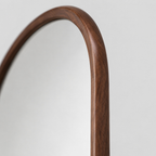 Close up of the natural wood grain along the walnut frame surface of the arched solid wood full-length mirror.