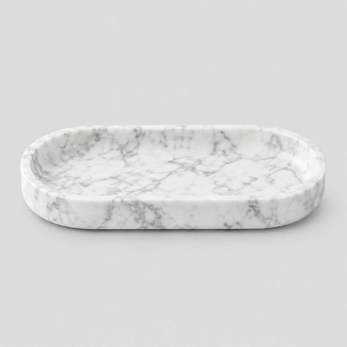 Oval carved stone catchall tray in Carrara White on a light gray studio background.