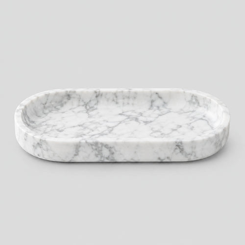 Oval carved stone catchall tray in Carrara White on a light gray studio background.