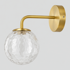 Brass wall sconce with a curved arm and hammered glass globe on a light gray studio background.