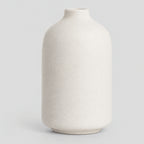 Off-White matte ceramic bud vase standing alone on a light neutral gray studio background.