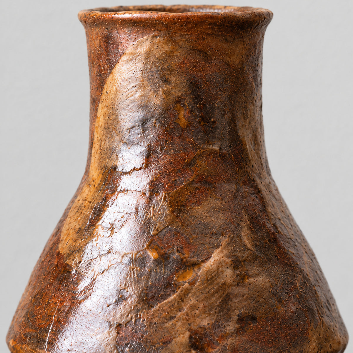 Close up of the textured rustic glaze across the tapered body of the coarse pottery bud vase.