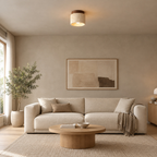 Cylindrical travertine flush mount ceiling light in walnut finish lit on the ceiling above a 200 cm wide sofa.