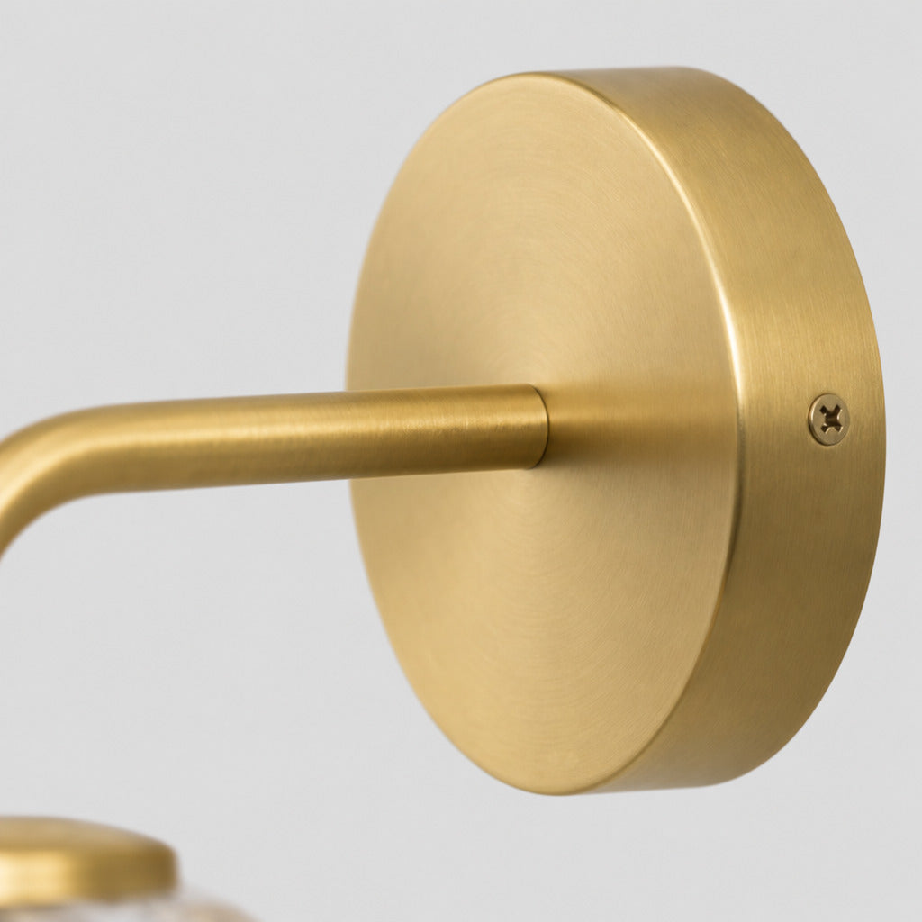 Close up of the round canopy against the wall on the brass wall sconce.