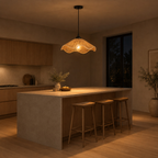 Wavy woven rattan pendant light lit in the evening hanging above a 180 cm long kitchen island, the only light in the room
