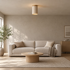 Cylindrical travertine ceiling light lit on the ceiling above a 200 cm wide sofa against greige plaster walls.