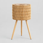 Standing woven rattan planter basket on wooden tripod legs in Natural Rattan on a light gray studio background.