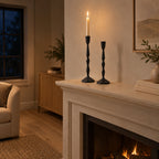 Set of two faceted cast iron taper candle holders in Matte Black on a 140 cm wide mantelpiece above a fireplace with one lit taper candle in the holder