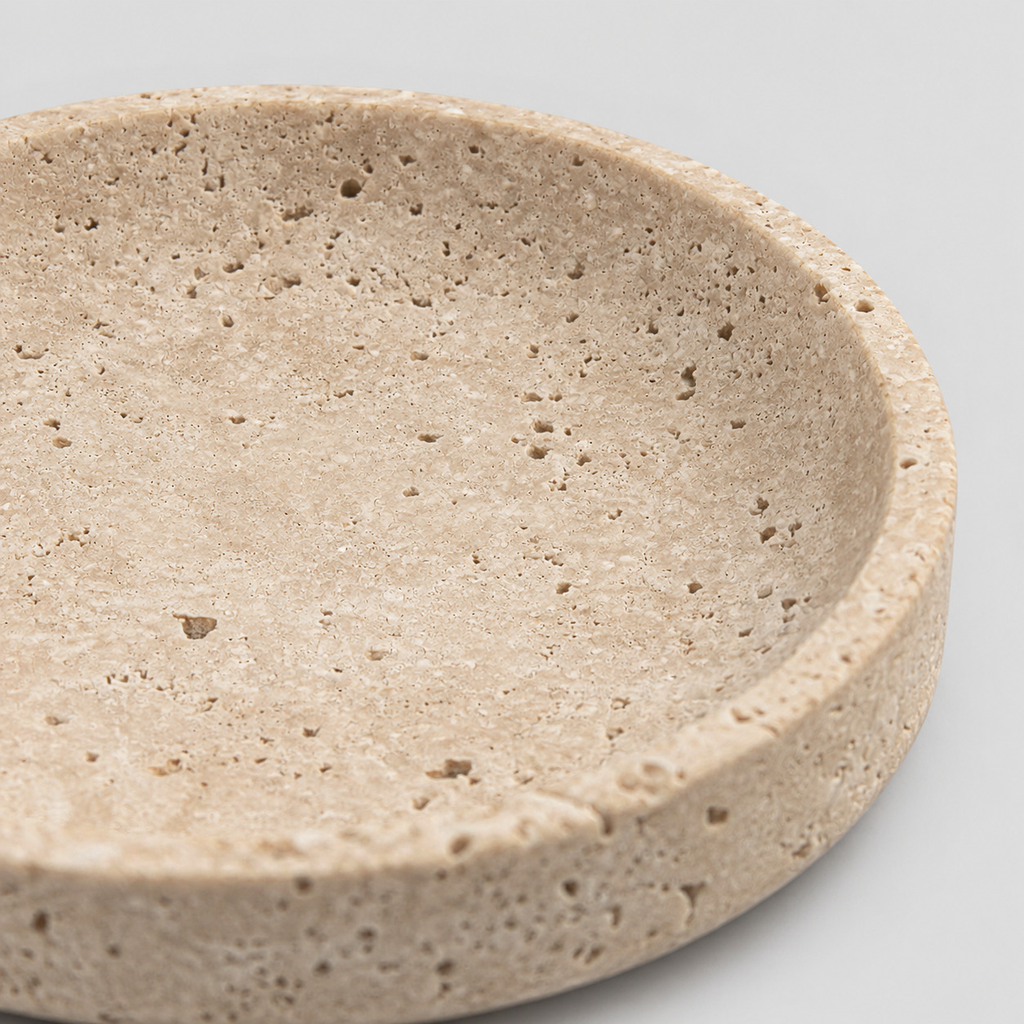 Close up of the porous honed surface texture of the round beige travertine dish