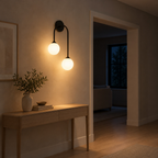 Matte Black asymmetric double-globe arch wall sconce lit in the evening beside an 80 cm wide doorway, the only light in the room.