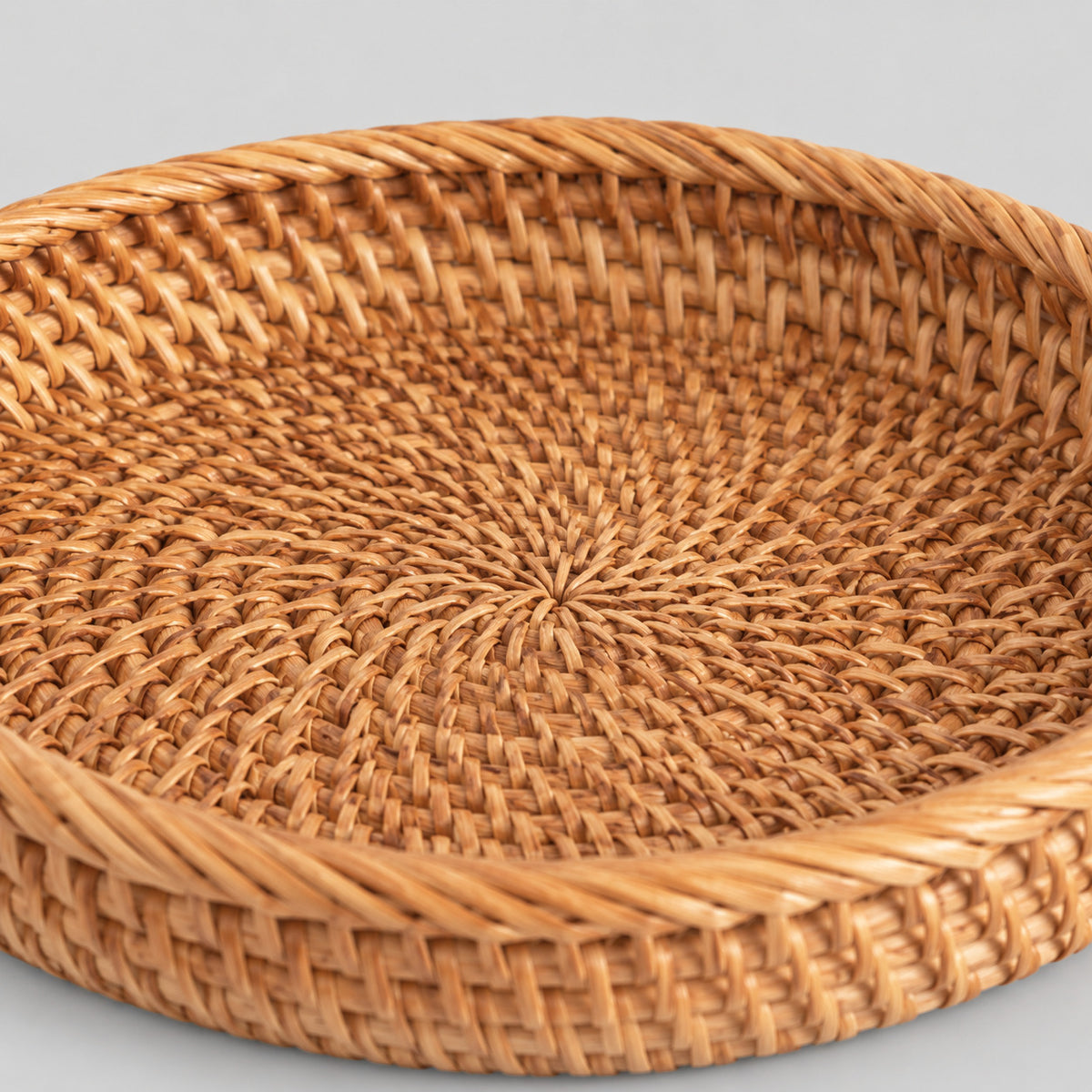 Close up of the tight spiral weave across the base of the shallow round woven rattan basket tray in Natural Rattan.