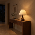 Walnut table lamp lit in the evening standing on a 120 cm wide walnut console table in a hallway, the only light in the room.
