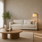 Matte Black arched floor lamp lit standing on the floor beside a 200 cm wide cream linen sofa.