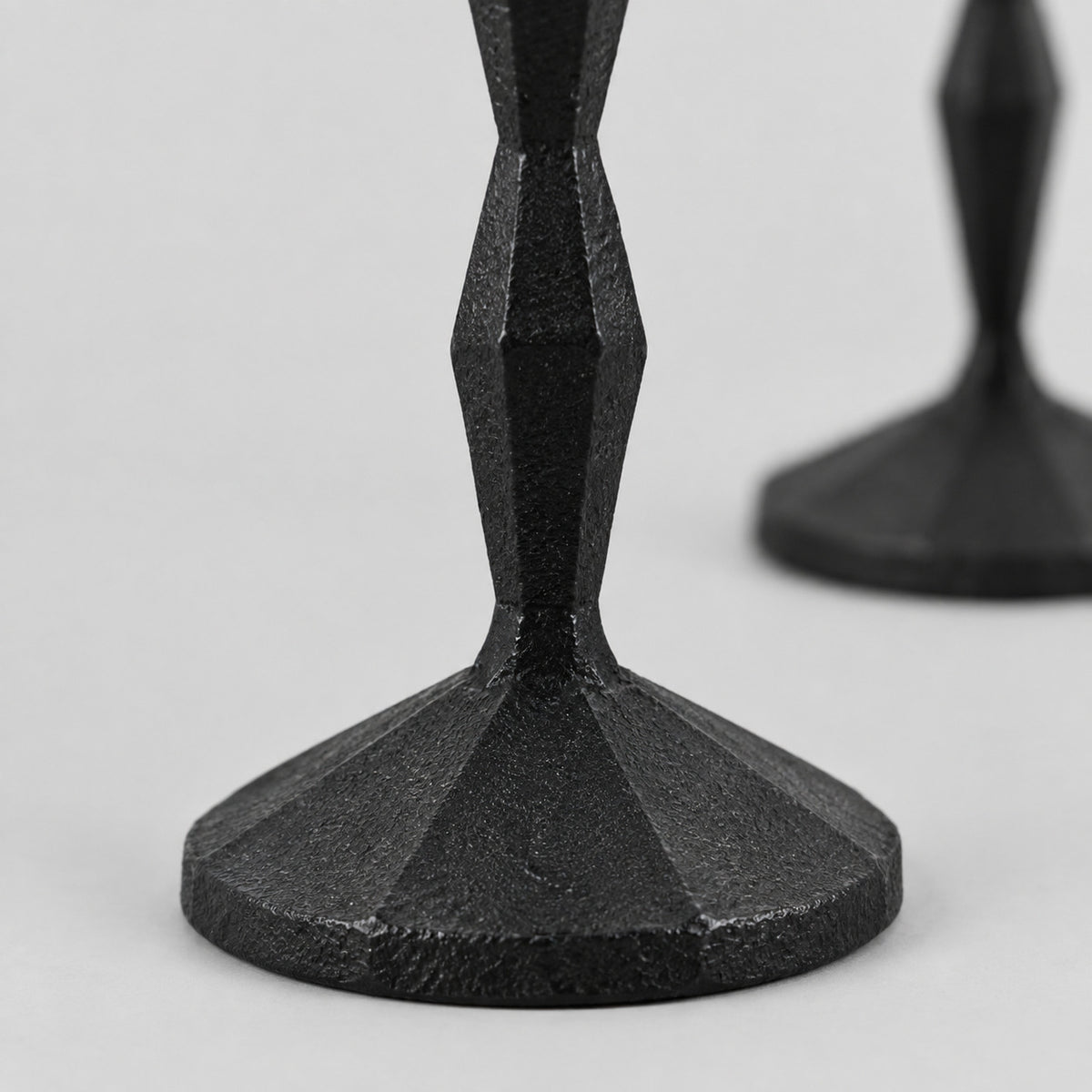Close up of the textured round base of the set of two faceted cast iron taper candle holders