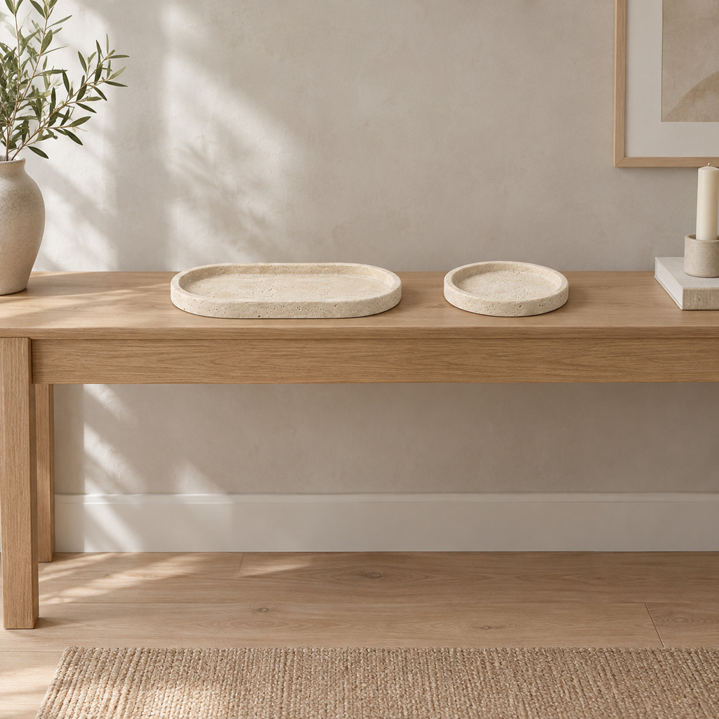 Round beige travertine catchall tray on a 120 cm wide oak console table in a calm room.