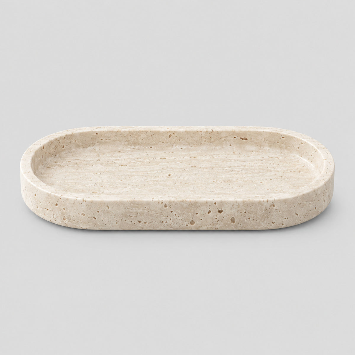 Oval carved stone catchall tray in Travertine on a light gray studio background.