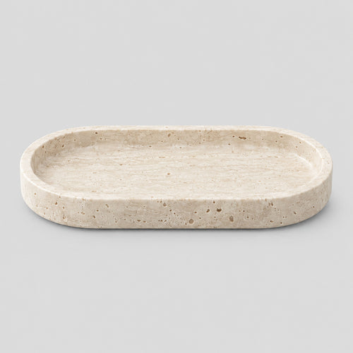 Oval carved stone catchall tray in Travertine on a light gray studio background.