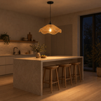 Wavy rattan pendant light lit in the evening hanging above a 180 cm long kitchen island, the only light in the room.