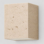 Travertine block wall sconce in travertine on a light gray studio background, in its Cube shape