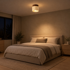 Cylindrical travertine flush mount ceiling light in walnut finish lit in the evening on the ceiling of a bedroom above a 160 cm wide made bed, the only light in the room.