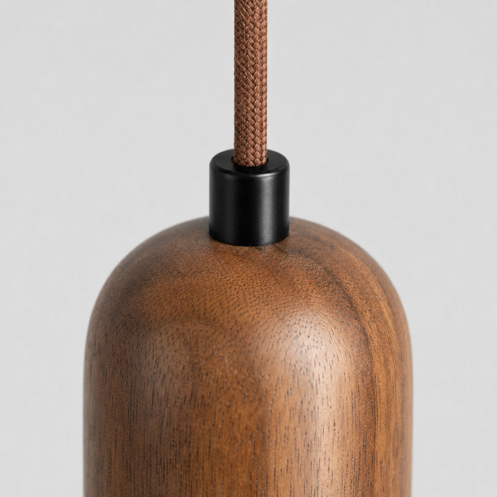 Close up of the cord grip where the suspension wire enters the walnut socket cap of the yellow travertine pendant light.
