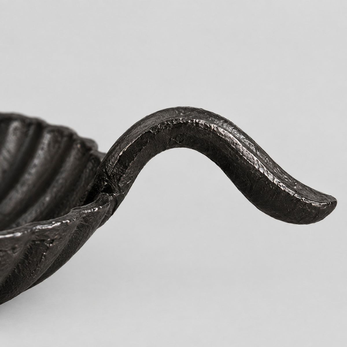 Close up of the curved cast iron finger handle of the chamberstick candle holder.