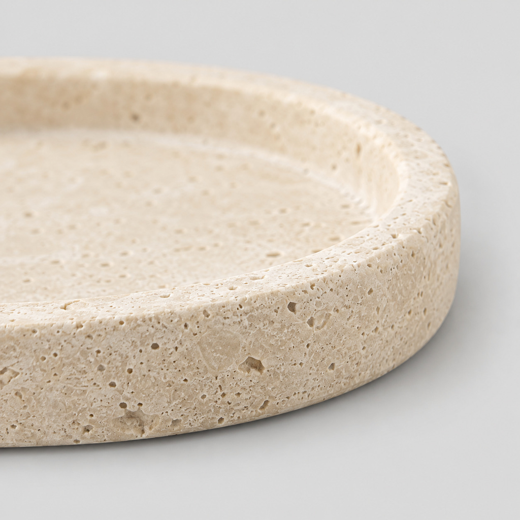 Close up of the rounded carved stone rim of the round beige travertine catchall tray.
