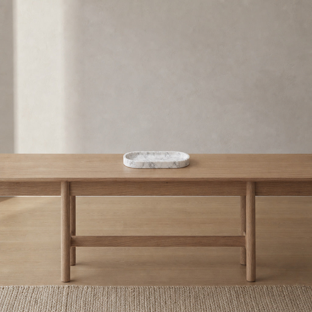Oval carved stone catchall tray in Carrara White on an oak console table in a calm room.