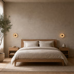 Round travertine disc wall sconce lit mounted on the plaster wall beside a 150 cm wide double bed, at headboard height