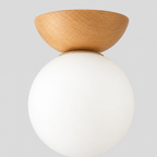 Natural wood flush mount ceiling light with an opal glass globe shade on a light gray studio background.