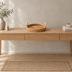 Natural rattan round woven serving tray on an oak console table in a calm room.