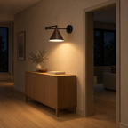 Walnut swing-arm wall sconce lit in the evening mounted on the plaster wall of a hallway beside an 80 cm wide doorway, the only light in the room.
