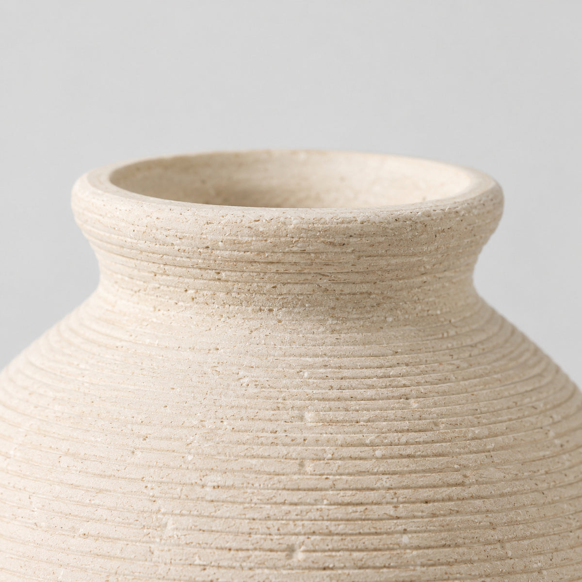 Close up of the smooth rounded rim at the opening of the off-white ceramic vase.