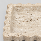 Close up of the porous surface texture of the travertine of the scalloped square stone tray in Yellow Travertine.