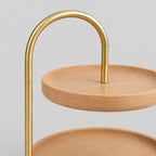 Close up of the arched brushed brass handle of the two-tier round wooden serving tray in Beech.