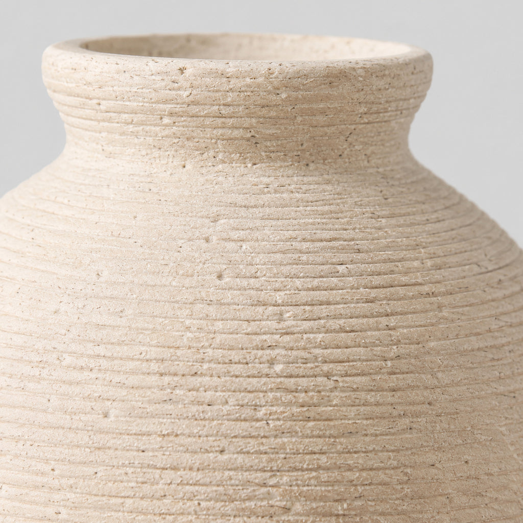 Close up of the carved horizontal ribbed pattern across the body of the off-white ceramic vase.