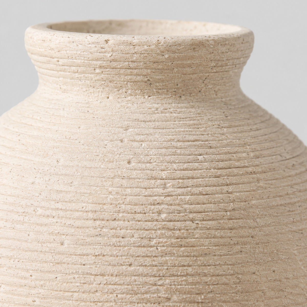 Close up of the carved horizontal ribbed pattern across the body of the off-white ceramic vase.