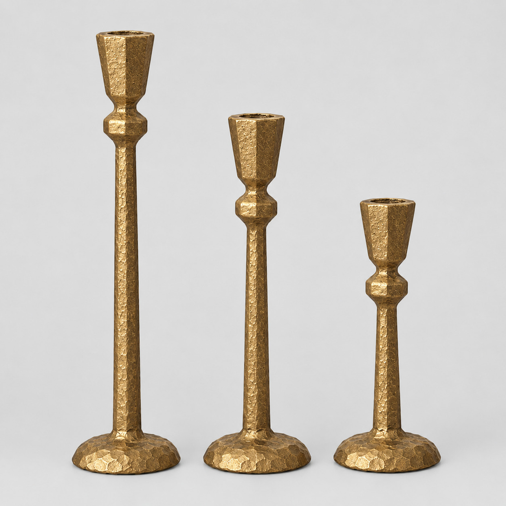 Set of three antique gold cast-iron taper candle holders in graduated heights on a light gray studio background.