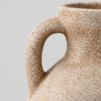 Close up of the curved ceramic loop handle where it connects to the flared neck of the ceramic amphora vase.