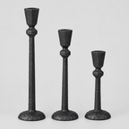 Set of three matte black cast-iron taper candle holders in graduated heights on a light gray studio background.