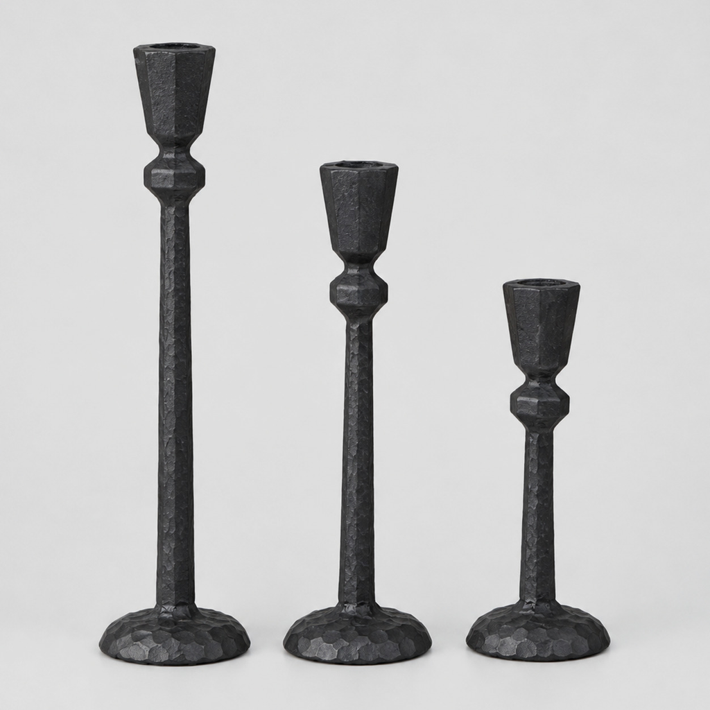 Set of three matte black cast-iron taper candle holders in graduated heights on a light gray studio background.