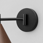 Close up of the round canopy against the wall of the walnut swing-arm wall sconce.