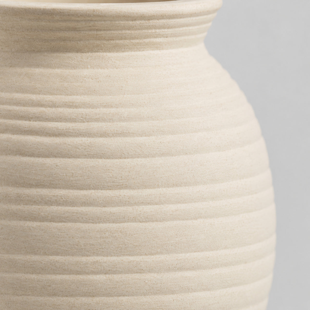 Close up of the horizontal ribbed texture of the off-white ceramic vase.