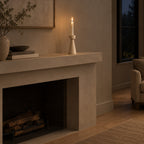 Travertine stone candle holder on a mantelpiece above a fireplace with one lit taper candle in the holder
