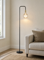 Brass socket floor lamp lit beside a sofa against a plain wall