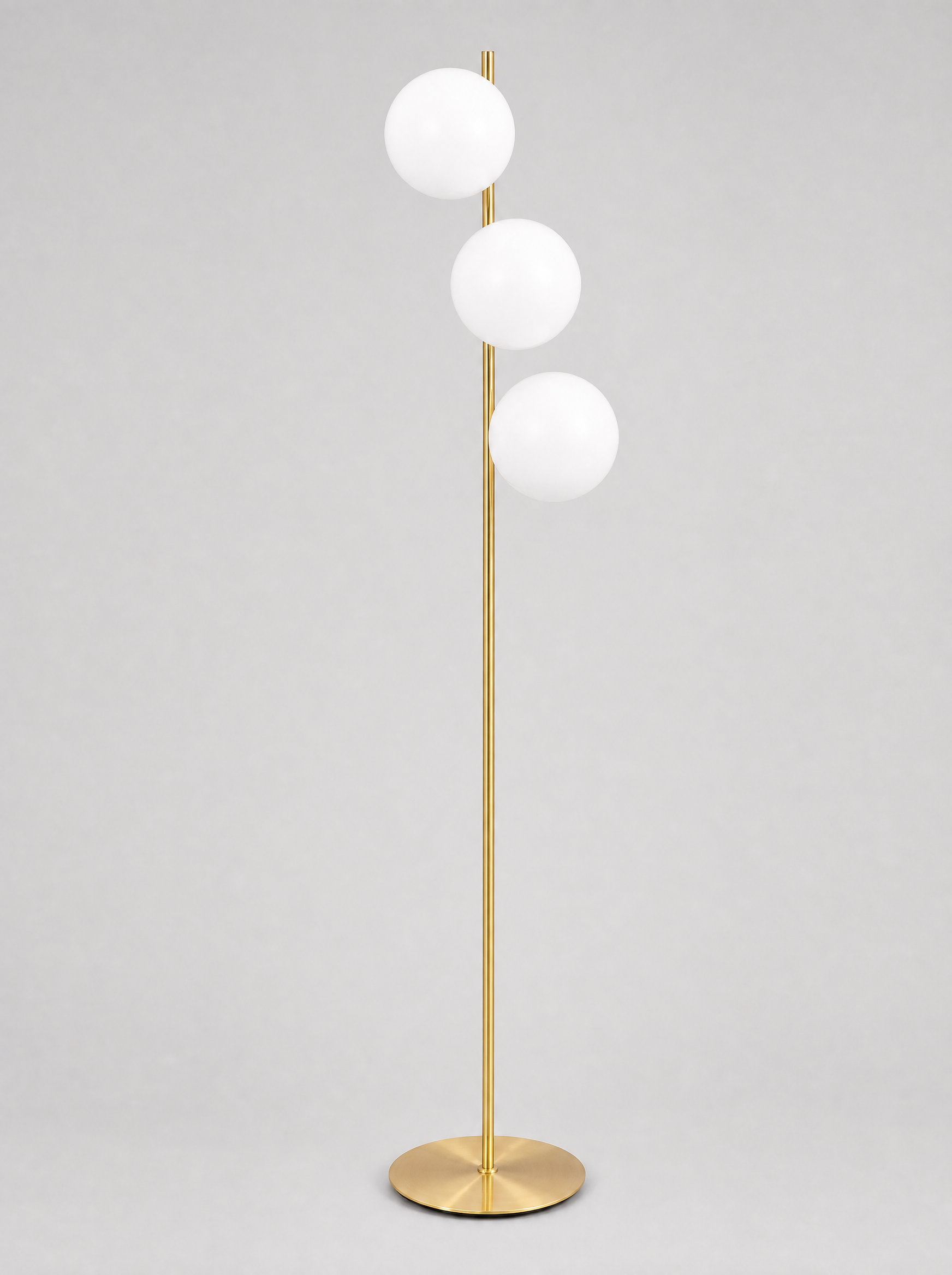 Brass floor lamp with three opal glass globes on a light gray studio background