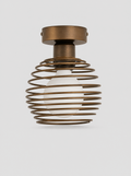 Black coiled metal flush ceiling light with an opal glass globe on a light gray studio background
