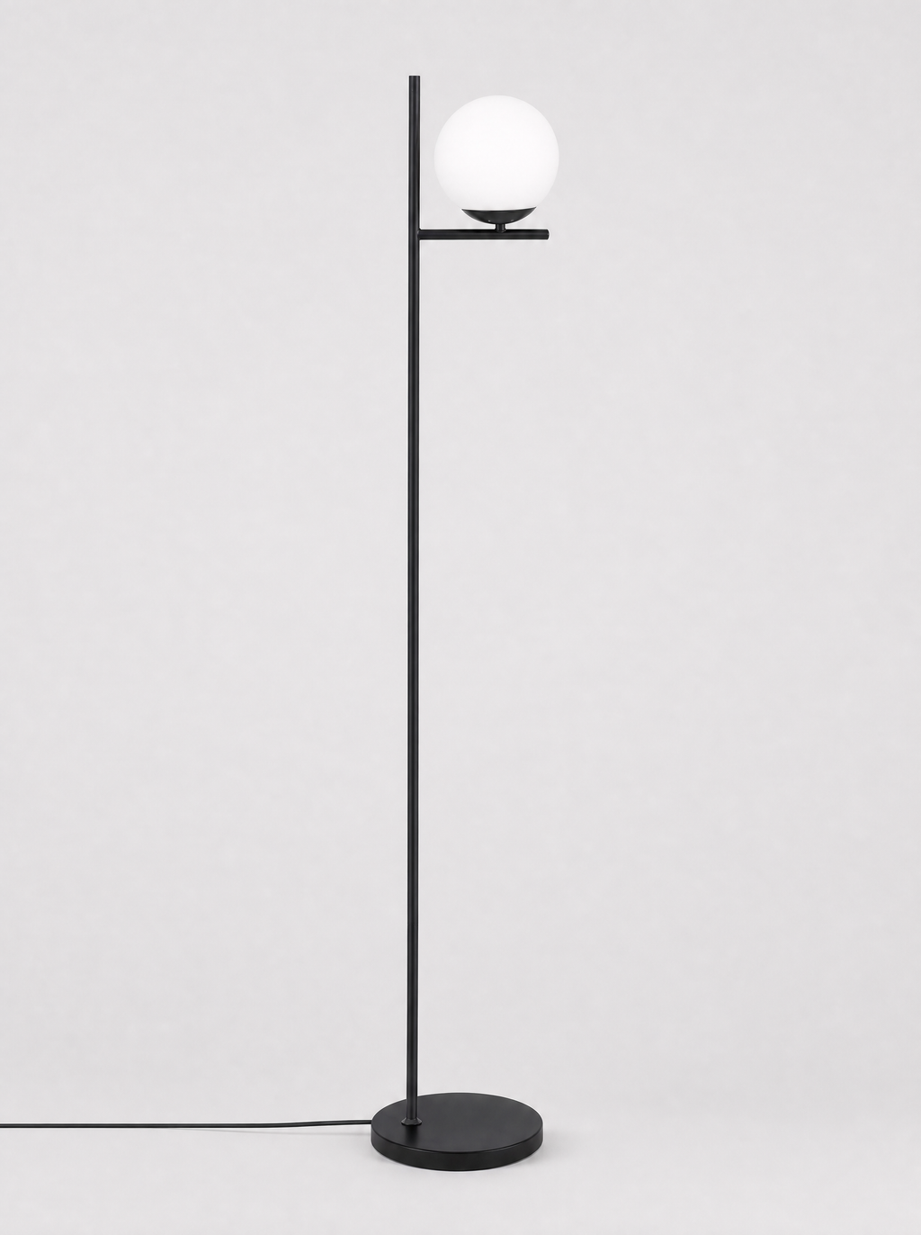 Black floor lamp with a single opal glass globe on a light gray studio background