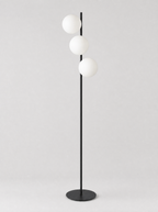 Black floor lamp with three staggered opal glass globes on a light gray studio background