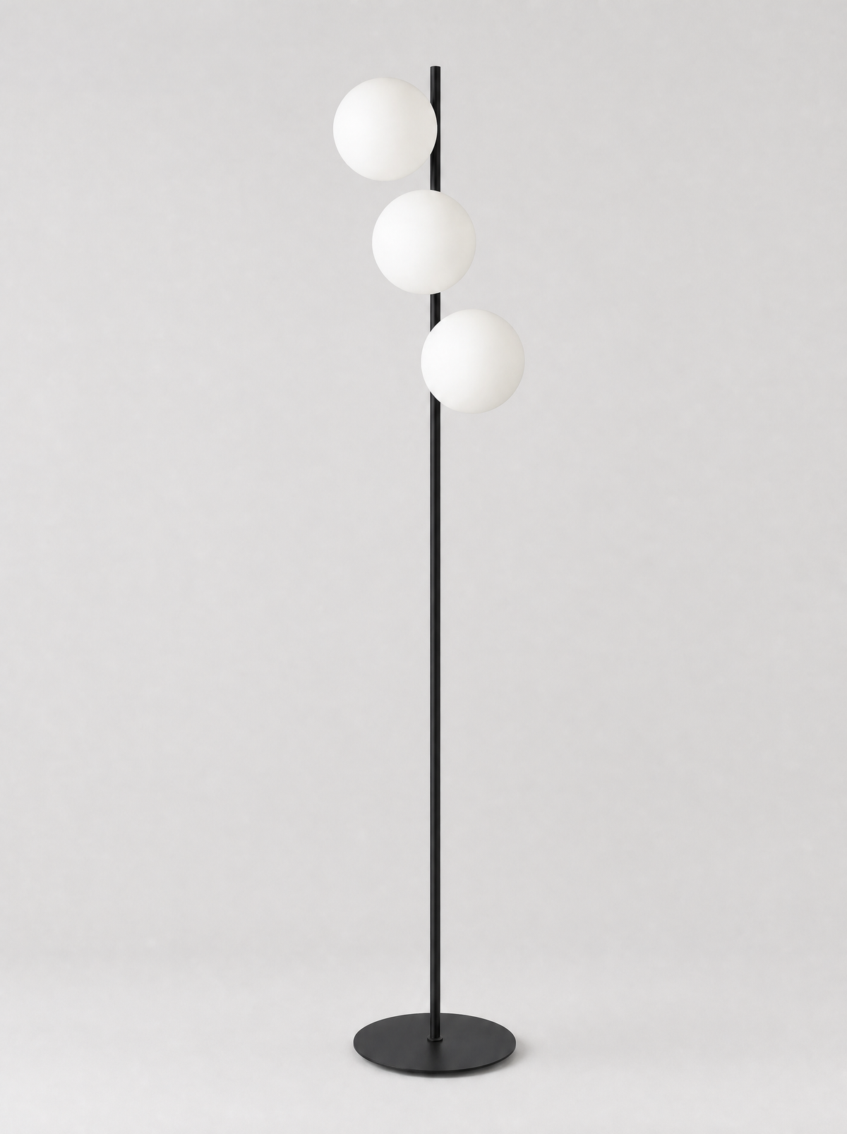 Black floor lamp with three staggered opal glass globes on a light gray studio background